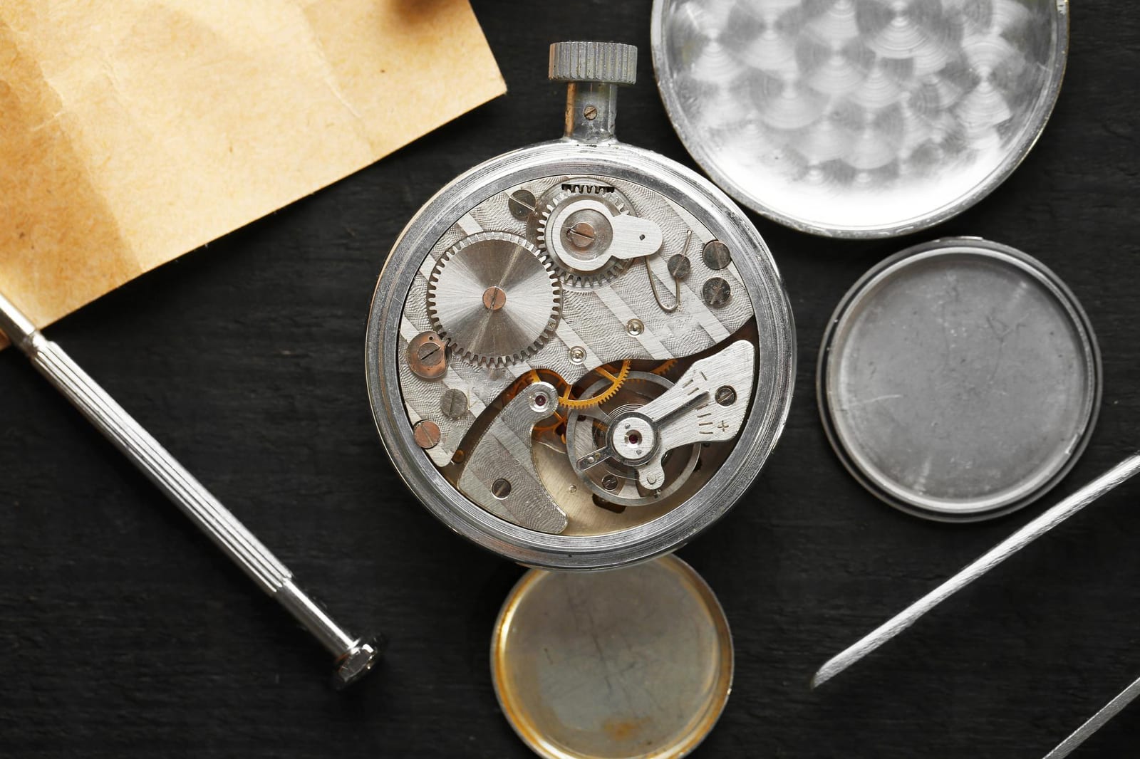 Movimento di un orologio da tasca aperto, con ruote e viti a vista accanto ai fondelli smontati